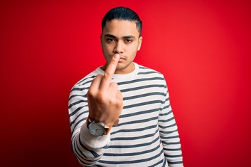 Young brazilian man wearing casual striped t-shirt standing over isolated red background Showing...