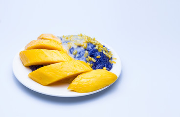 Mango sticky rice, purple glutinous rice from butterfly pea flower, topped with soy beans and coconut milk, Thai summer dessert. Put the dish on the white ground