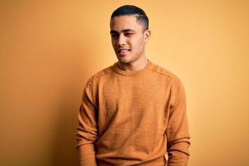 Young brazilian man wearing casual sweater standing over isolated yellow background winking looking...