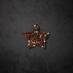 Peppercorn pepper on a black background, laid out in the shape of a star. Red, white, green and...