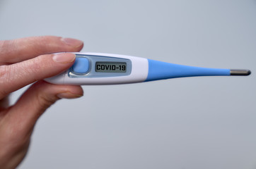 Male hand holds clinical thermometer with covid-19 text on the screen during global covid-19 or corona pandemic