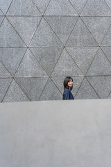 In front of the gray wall, young business women smile to the camera