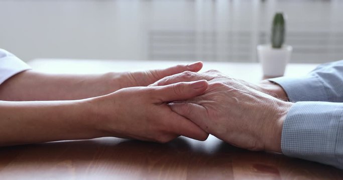 Young woman adult daughter or doctor, caregiver, medical nurse holding old man hands of senior father patient on table. Elderly people health care, support, medicare and comfort concept. Close up view