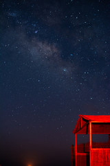 Starry sky with a galaxy over a red-lit wooden hut