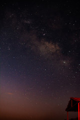 Starry sky with a galaxy over a red-lit wooden hut