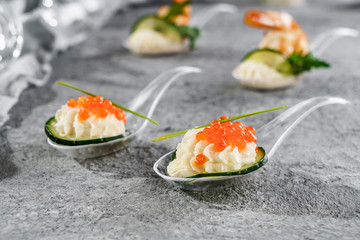 Delicious appetizers with red caviar and cheese mousse in glass spoon on grey banquet table. Gourmet food close up, snack, antipasti, close up