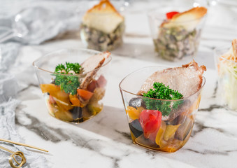 Delicious appetizers in glass cups with ham meat and grilled vegetables on marble banquet table. Catering food, canape and snacks, close up