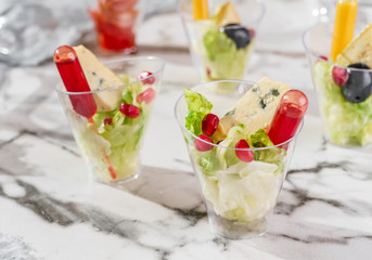 Delicious appetizers in glass cups with lettuce, pomegranate sauce, blue cheese on marble banquet table. Catering food, canape and snacks, close up