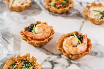 Delicious appetizers in tart with shrimp on marble banquet table. Catering food, canape and snacks, close up