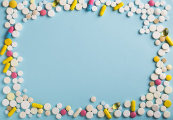 Assorted pharmaceutical medicine pills, tablets and capsules in office. Blue background.