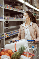 woman with medical facemask looking at empty shelves in a supermarket.
