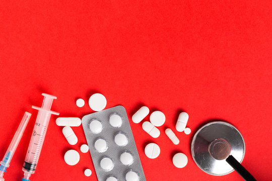 Assorted pharmaceutical medicine pills, tablets and capsules. Red background.