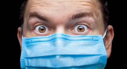 portrait of a man in a medical mask with wide-open surprised eyes, close up of a face with shock emotion from the consequences of the coronovirus covid 19 pandemic.