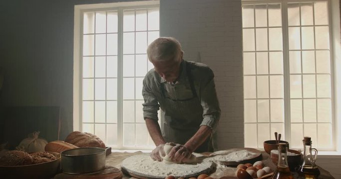 Professional senior moustached caucasian baker working in bakery shop in morning, kneading dough for bread, using traditional recipes, elderly man enjoying his hobby after retiring 4k footage