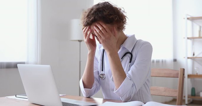 Stressed upset young female doctor feeling worried about professional malpractice. Depressed tired physician regrets medical diagnosis mistake suffers from guilt or headache sitting alone in office.