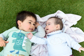 Hermanos felices tumbados sobre cesped verde