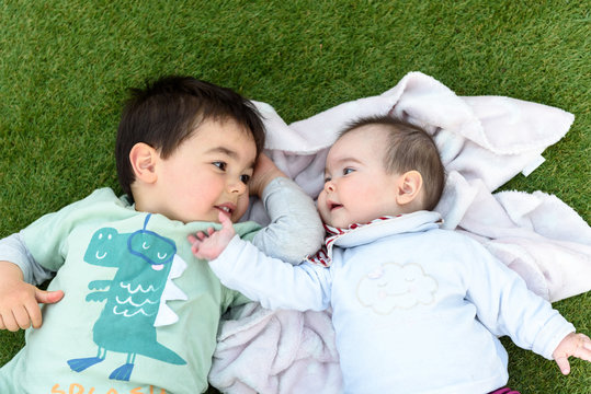 Hermanos felices tumbados sobre cesped verde