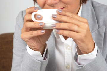 Business woman drinks coffee from a white cup close-up