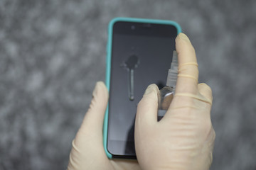 Hand of woman is spraying alcohol,disinfectant spray on mobile phone,prevent infection of Covid-19 virus,contamination of germs or bacteria,wipe or cleaning phone to eliminate,outbreak of Coronavirus