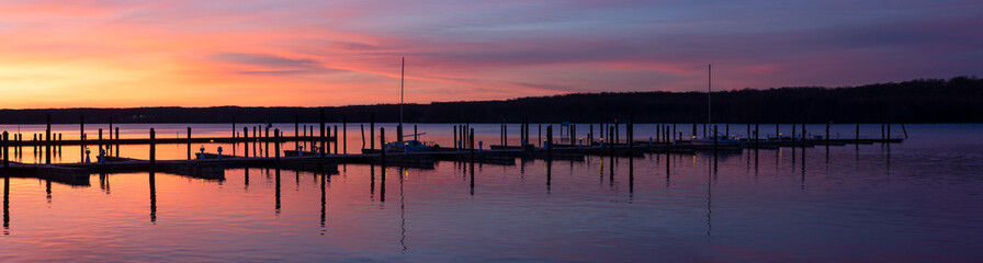 Fototapeta premium Marina Dock Panorama at Dawn with Sun Rising to a Pink and Purple Clouded Sky Over a Calm Tree Lined River