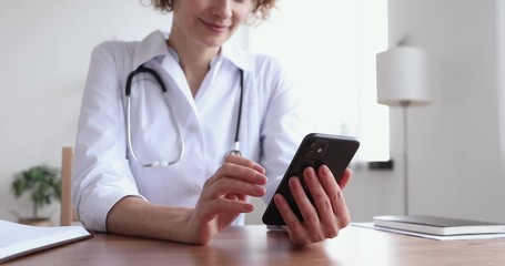 Female doctor wearing white coat holding cell using smart phone apps texting message to remote patient. Practice of medicine and public health care supported by mobile devices concept. Close up view