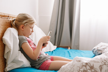 Cute adorable Caucasian girl stay at home and call friends on smartphone. Child kid having face time call talk with people relatives while on self isolation during quarantine of COVID-19.