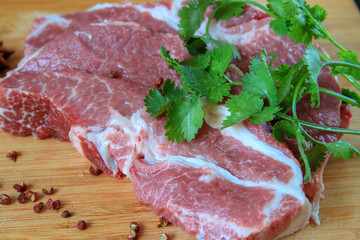 Pork on the bamboo cutting board with pepper and cilantro on the side