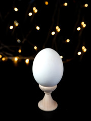 a white unpainted egg on a stand on a black background against a background of many yellow lights