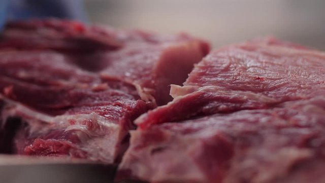 butcher in blue gloves cuts pork meat with knife on table