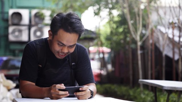 Young man with backpack using his mobile phone at a table outdoor.