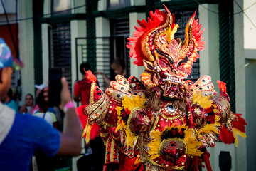 people take photos of man in vivid costume passing by city street at dominican carnival