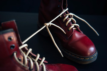 Stylish red shoes with laces tied together on black background, selective focus. High boots with shoelaces connected together, close-up. April Fool?s Day Shoes, joke, prank.