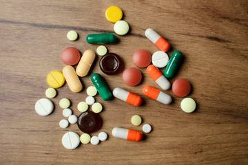 A handful of different pills on a wooden table. A lot of colorful different pills including...