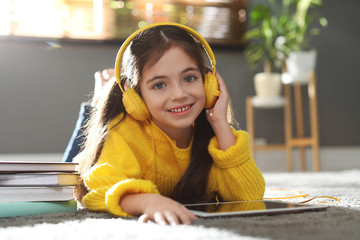 Cute little girl with headphones and tablet listening to audiobook at home