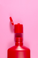 red open shampoo bottle and a cap over it on a pink background with empty place for text. vertical view