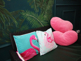 The pillows feature two flamingos with a pink heart-shaped pillow on a contrasting dark colored sofa and painted wall in plant pictures