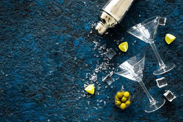 Bar background with martini glasses, shaker, ice, lemon and olives on blue table top-down copy space