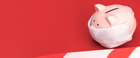 Banner. Pink Piggy Bank stands  on a  red background wearing medical face mask, the red and white...