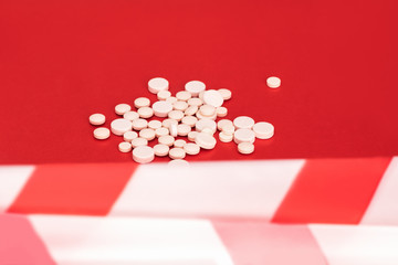 Tablets. A lot of white pills on a bright red background, a red and white ribbon stretched in front...
