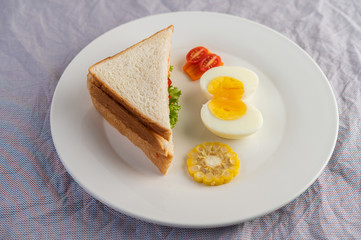 American breakfast on a white background with boiled eggs, corn, tomato and sandwich on a white plate.