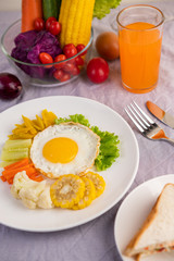 American breakfast on a white background with fried egg, salad, pumpkin, cucumber, carrot, corn, cauliflower, tomato, toast and orange juice.