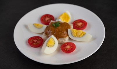 Bread topped with chili paste with boiled eggs and tomatoes on a white plate.