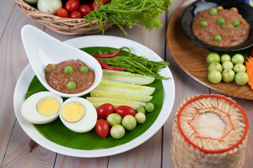 Chili paste paste in a bowl with eggplant, carrots, chili, cucumbers in a basket on wood table