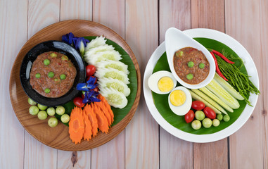 Chili paste paste in a bowl with eggplant, carrots, chili, cucumbers in a basket on wood table
