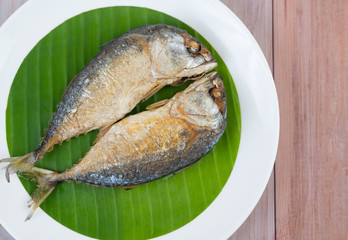 Fried mackerel placed on a white plate on a wooden floor