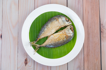 Fried mackerel placed on a white plate on a wooden floor