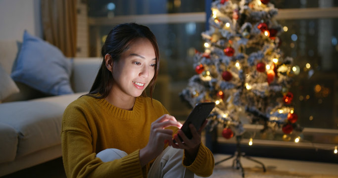 Woman use of cell phone with christmas tree decoration at home