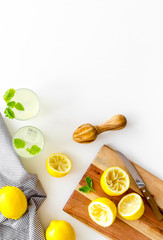 Homemade lemonade in glasses near juicer and cut lemons on white background top-down copy space