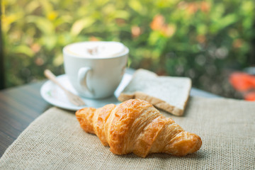 Freashly baked tasty croissants with coffee cup on wooden background.