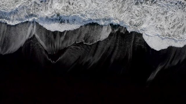 Waves from Atlantic ocean breaking on a black sand beach, top down aerial.